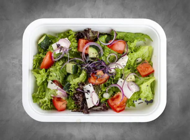 Photo of Greek salad with feta cheese. Healthy diet.Takeaway food. Top view, on a gray background.