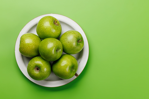 Plate with fresh green apples over green background. Flat lay with copy space