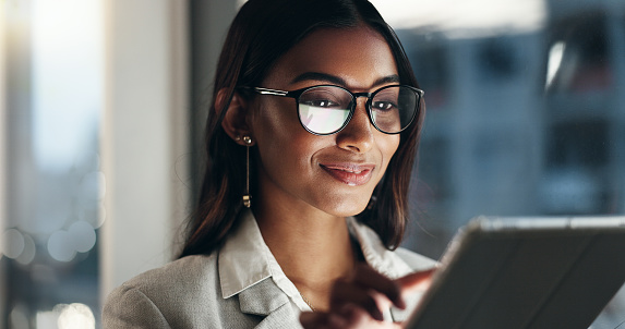 Tablet, overtime and happy woman in office with glasses, reflection with planning and website. Vision, smile and businesswoman typing email, late at night work and research on future ideas for agency