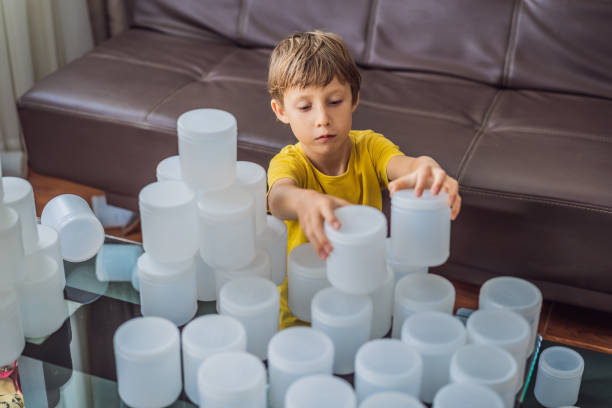 boy playing with cans of yogurt surrounded by many jars of yoghurt that he uses in a year. a huge amount of plastic food jars. excessive consumption of plastic. reduce, reuse, recycle - resume garbage heap rejection zdjęcia i obrazy z banku zdjęć