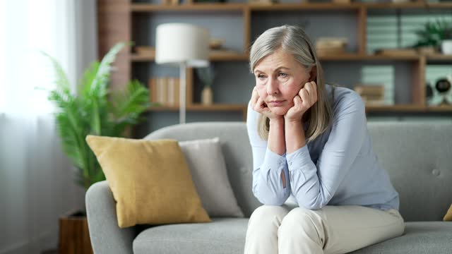 Senior gray haired female has depression suffering from mental pain sitting on the sofa in living room at home.