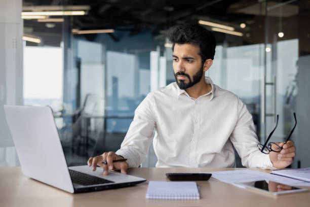 istock Serious and focused young Indian man working in office at desk, typing on keyboard, processing data and searching for information 2032326113