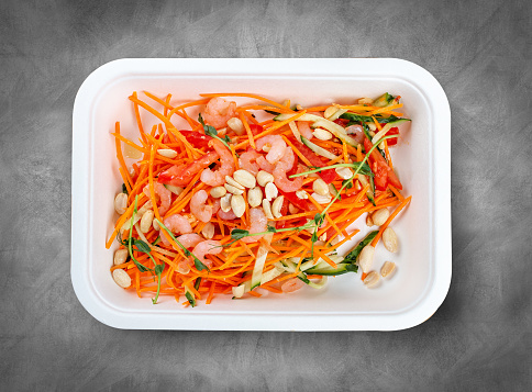 Salad with shrimp and chopped vegetables. Healthy diet. Takeaway food. Ecological packaging. Top view, on a gray background.