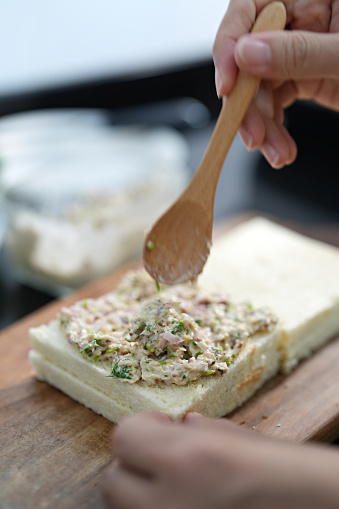 In the cropped shot, a woman is seen preparing a tuna sandwich in the kitchen.