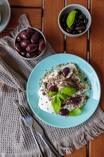 Feta cheese sliced on blue plate with sesame, flax seeds, served with black olives and basil leaves. Delicious and healthy breakfast on terrace