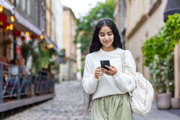 istock A young smiling Indian woman with a backpack uses a mobile phone while walking on a city street 2032363362