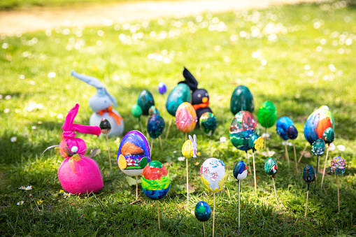 Easter eggs and Easter bunnies painted with paints and sparkles by children's hands lie on the lawn on a sunny spring day in the park. Happy Easter and Easter Egg Hunt. Do it yourself.