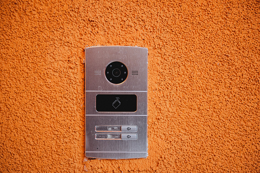 Metal intercom system with silver finish on terracotta wall. Camera, speaker, call button, and access card reader included. Access card reader covered by small door.