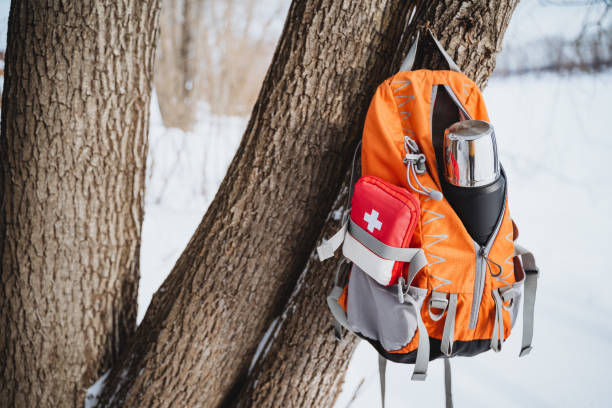 Orange backpack with a first aid kit and a thermos hangs on a tree in the winter forest.