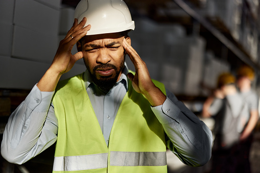 Frustrated African American inspector having a headache while working in a storage room.