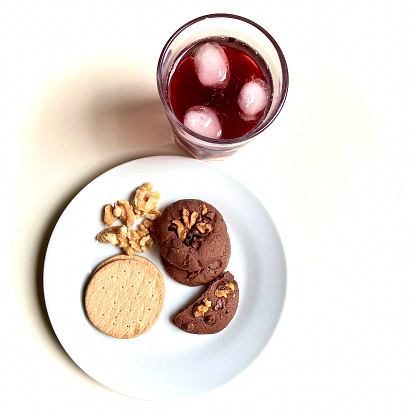 Above view of chocolate cookies in a white plate with infusion of Jamaica flower tea with ginger and cinnamon stick with ice.