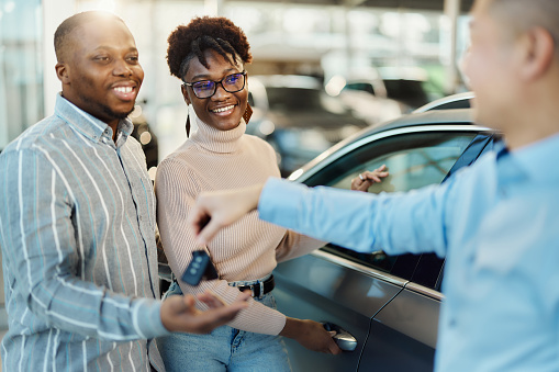 Happy African American couple receiving new car keys from a salesman in a showroom. Focus is on woman.