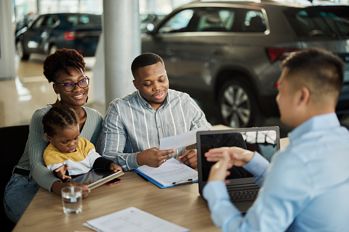 Happy African American family communicating with male salesperson during a meeting in a car showroom.