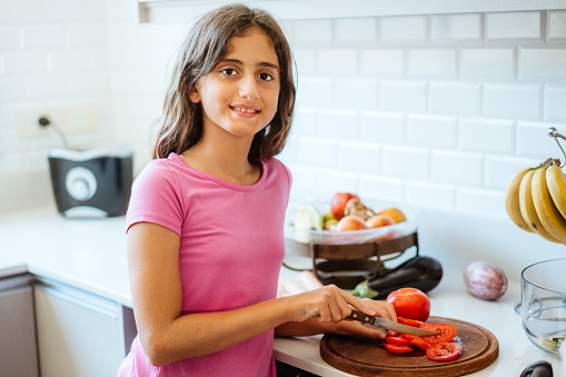 Cheerful preteen slicing tomatoes on a cutting board, surrounded by fresh ingredients at home.