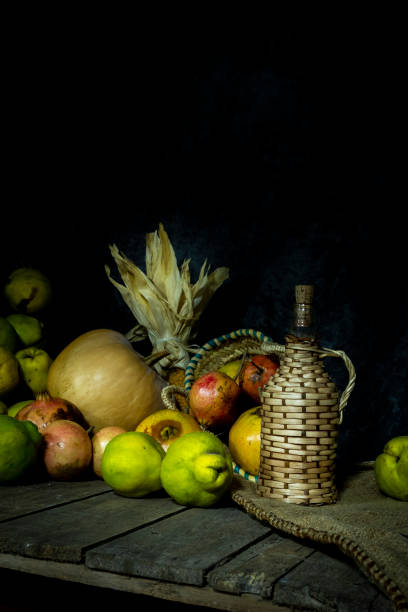 istock Autumn still life with different fruits such as pumpkin, grapefruit, pomegranate, corn and persimmons next to a traditional wooden covered bottle on wooden table and dark background. Vertical. 2032423662