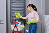 Woman doing house cleaning in bathroom, cleaning dust from heated towel rail