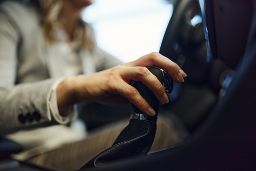 Close up of unrecognizable woman holding her hand on a gearshift while driving a car.
