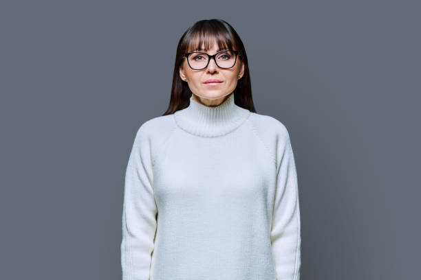 istock Middle-aged beautiful serious woman in white sweater on gray studio background 2032437028