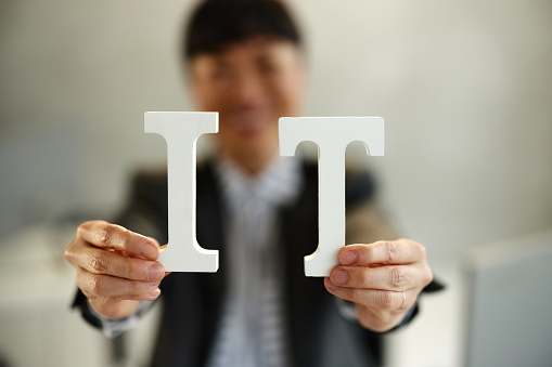 Close up of unrecognizable businesswoman holding letters I and T as a concept of internet technology in the office. Copy space.