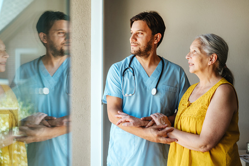 Healthcare professional in scrubs comforting elderly female patient in bright room.