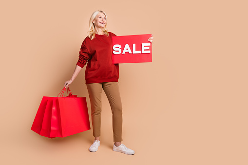 Full length photo of excited dreamy lady dressed red pullover holding shoppers sale card looking empty space isolated beige color background.