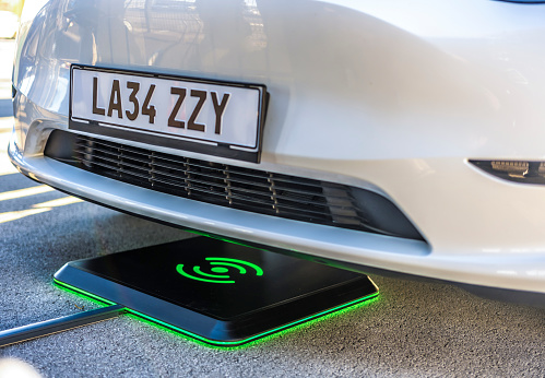 Close-up of electric car being charged with wireless charger under car bonnet.