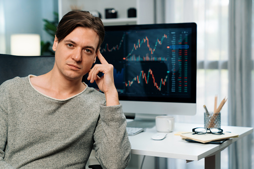 Smart business trader in casual looking at camera against value dynamic increased stock exchange market monitor screen backside, profile of investing financial businessman at modern office. Pecuniary.