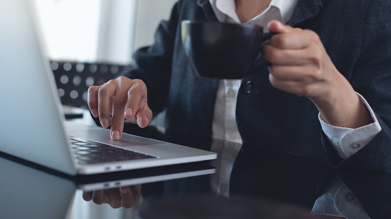 Business woman working on laptop computer, surfing the internet and drinking coffee at modern office, corporate business, close up