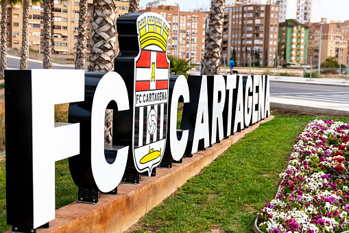Cartagena, Murcia - Spain - 01-16-2024: The FC Cartagena sign features the club's emblem amidst flowering plants
