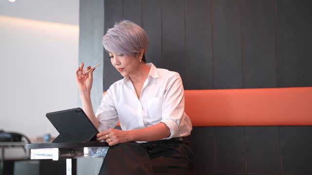 Senior Asian businesswoman, using her tablet to organize her schedule at a nearby cafe, close to her office
