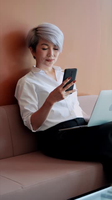 Senior Asian businesswoman, using her mobile phone to check work online at a cafe near her office