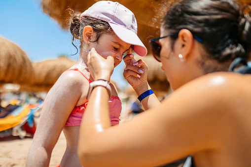 Young mother putting sunscreen on her daughter on the beach in Hurghada in Egypt.