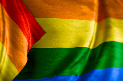 Full frame background of an LGBTQ+ pride flag moving in the wind. The traditional rainbow colored pride flag.