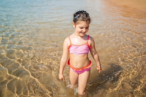 Toddler girl in yellow swimsuit sitting at the edge of pool