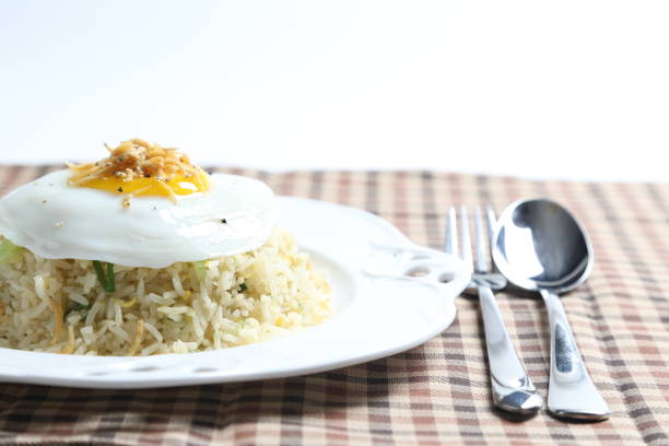 wok fried garlic olive egg rice with small silver fish seafood, fried egg and vegetables in plate on vintage table cloth white background asian chef cuisine halal food menu for cafe