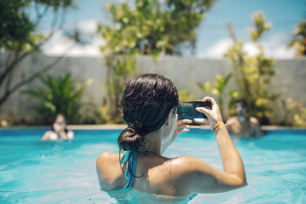 mulher nova que tira foto móvel na piscina no verão - mobilestock freedom enjoyment blue - fotografias e filmes do acervo