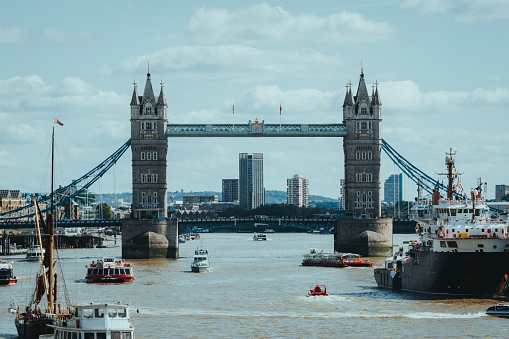 A Boat traffic moving along river with bridge in background, London, UK
