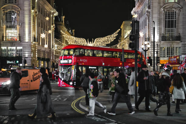 Piccadilly Circus, West End London, England, United Kingdom, Great Britain – 20th Nov. 2023: The Spirit of Christmas by Regent Street - famous glittering angels of Regent Street: London's iconic Christmas lights and A double-decker bus (double-deck bus) on the streets of the West End. A nighttime street view in London city during the Christmas time, festivities season. In the heart of London's festive season, around Piccadilly Circus, people are snapping photos with their phones to capture this Christmas cheer. in addition, the delightful Christmas lights near the St James area add to the joyful atmosphere. Folks are strolling around, enjoying the Christmas holiday spirit, and some cross the road in the lively West End London area.It was taken at the road junction and iconic public space of London's West End in the City of Westminster in the UK. A double-decker bus on Piccadilly Circus- Regent Street by Piccadilly.