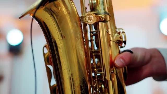 A saxophonist plays music at a concert indoors on stage. a golden saxophone in the hands of a male musician. Slow motion