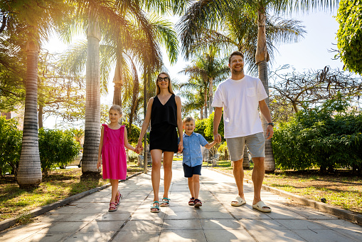 happy family with children walking in hands down an alley in a palm tree park in Tenerife, Spain. summer vacation