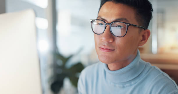 istock Asian man at computer, glasses and reflection, thinking and reading email, review or article at digital agency. Internet, research and businessman at tech startup with report, networking or feedback. 2032671642