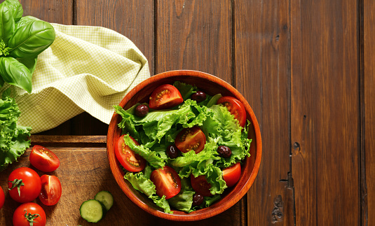 fresh salad with tomatoes and olives in a wooden bowl