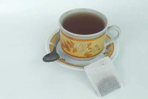 A tea in white ceramic cup with a luxurious floral pattern with a tea bag. Isolated in white background.