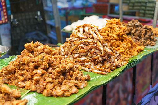 An enticing display of Thai street food featuring heaped mounds of crispy pork on banana leaves, showcasing the rich variety of textures and flavors, from juicy tenderness to golden crunchiness
