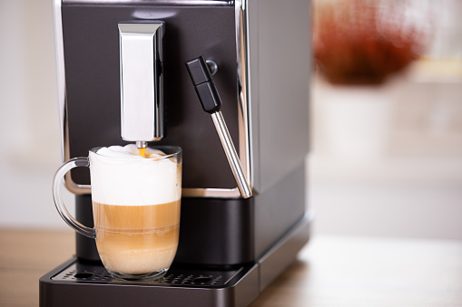 Photo that illustrates the process of making a cup of cappuccino in the coffee machine. The mix of the milk and froth with the coffee is shown in layers inside the cup of glass.