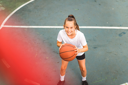 A portrait of a kid girl playing with a basketball in park