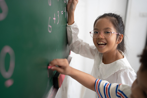 Happy Asia kid girl studying and writing with chalkboard and friend in classroom