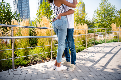 Cropped photo of charming sweet married couple dressed casual outfits embracing hands pockets walking outdoors urban city park.