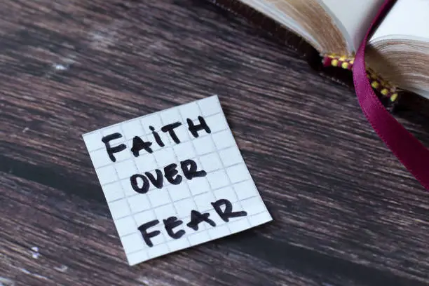 Faith over fear, handwritten text with open holy bible book on wood. Christian biblical concept of spiritual strength, courage, and trust in God Jesus Christ.