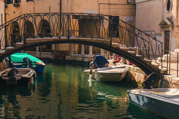 Venice, Veneto, Italy - 10/09/2020: A man working on is boat inside one of the canals of Venice
